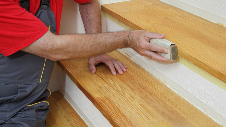 Man in overalls sanding wood stairs