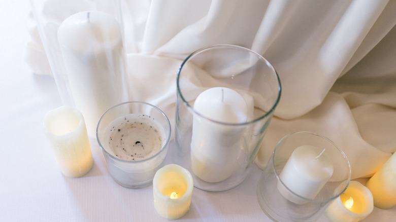 Plain pillar candles in glass vases are surrounded by some additional plain candles