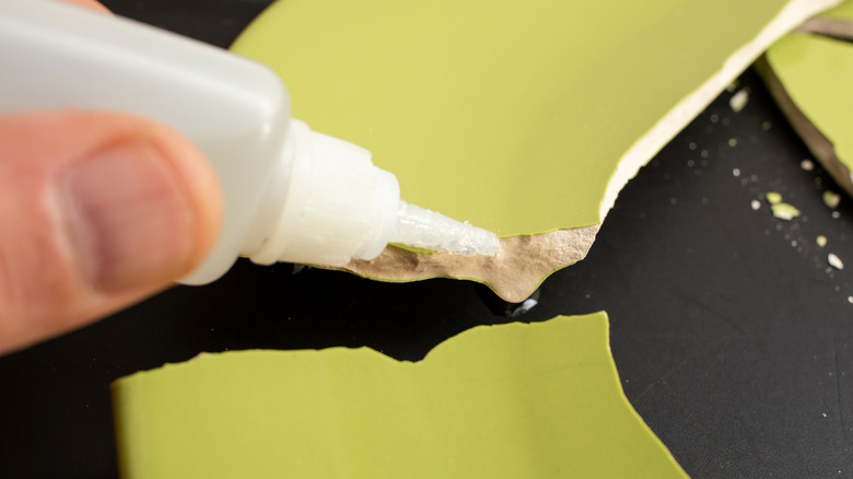 Close up of a hand applying glue to broken ceramic