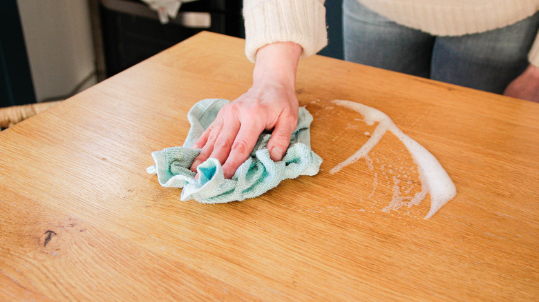 A person cleans a wooden surface using a cloth