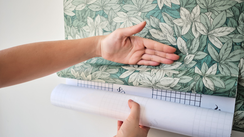 Hand applying a botanical wallpaper on a white wall