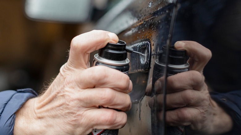 Man spraying lubricant on car door lock