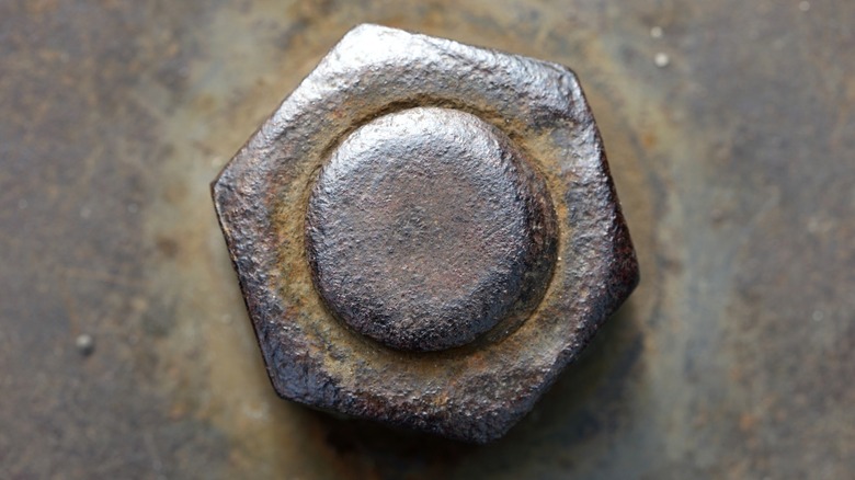 closeup of rust nut on bolt against rusty metal surface