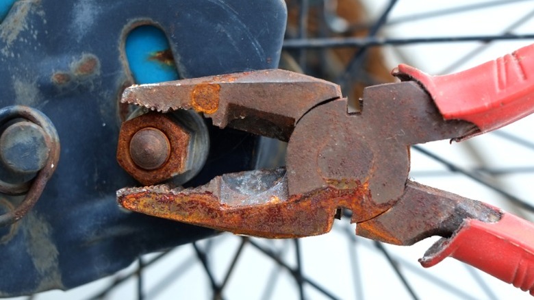 rusty red-handled pliers removing rusty nut from bicycle wheel