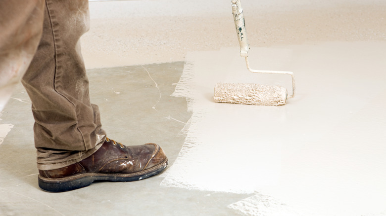 Person in work boots painting a white concrete floor with a roller