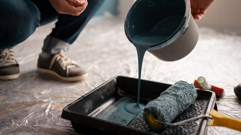 Person pouring dark blue paint from its can to a paint tray with a roller on it