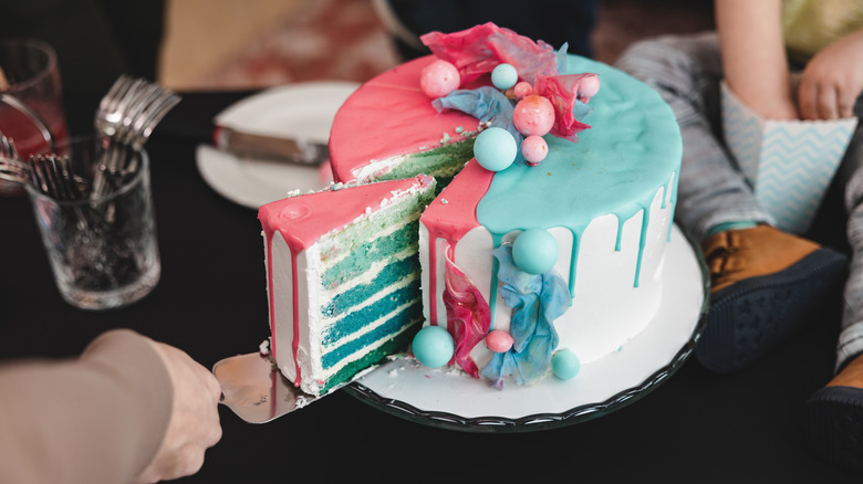 person cutting blue and pink cake