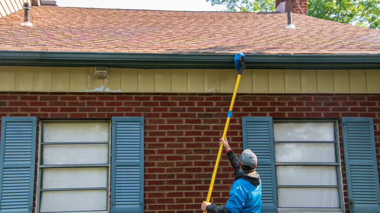 Person cleaning their home's gutter with a telescope brush