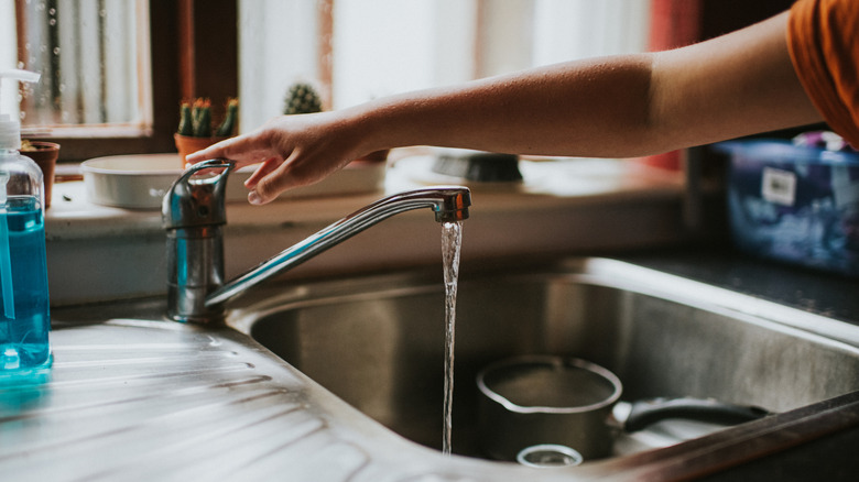 Hand resting on faucet at the kitchen sink