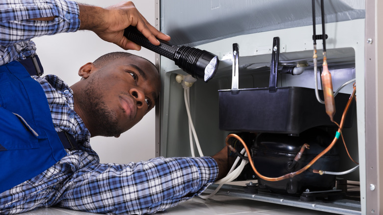 Man shining flashlight under fridge