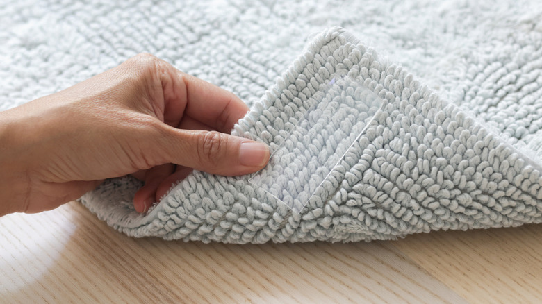 Woman's hand lifting corner of rug with tape beneath it