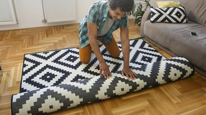 Man unrolling brightly patterned rug onto wood floor