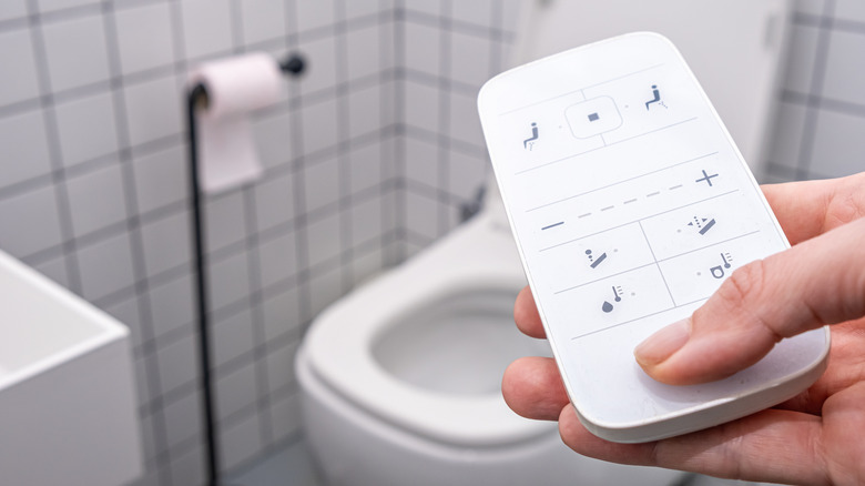 Person holding a remote to control a smart toilet