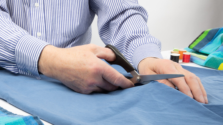 Hands cutting blue fabric with scissors