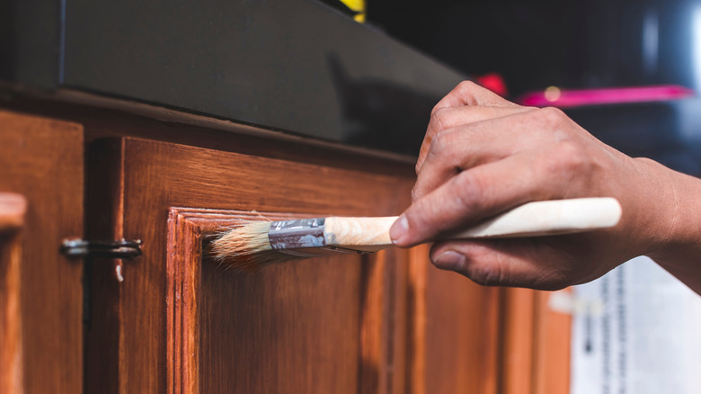 Hand holding paint brush painting directly onto installed kitchen cabinet door