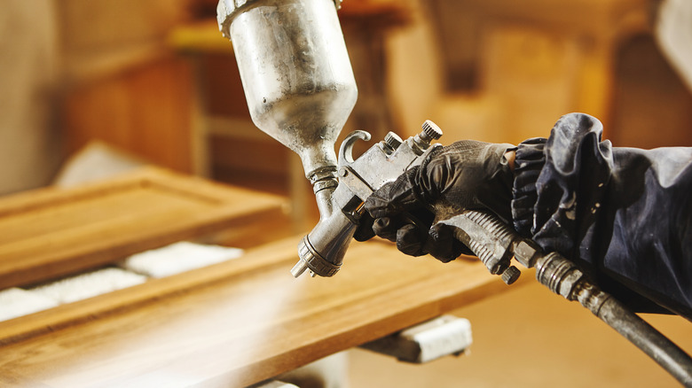 A person painting wood cabinets with a sprayer