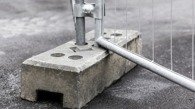 temporary metal fence secured by concrete block on tarred ground