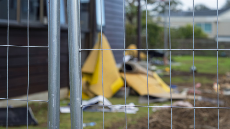 temporary fence protecting a residential home under construction with materials under tarp