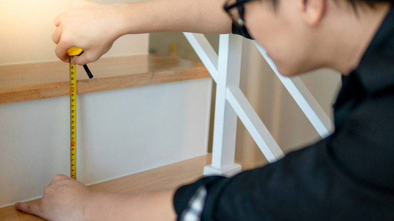 Person measuring stair riser with measuring tape