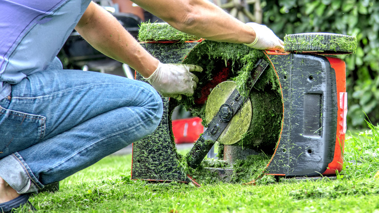 man cleaning grass from lawn mower blades