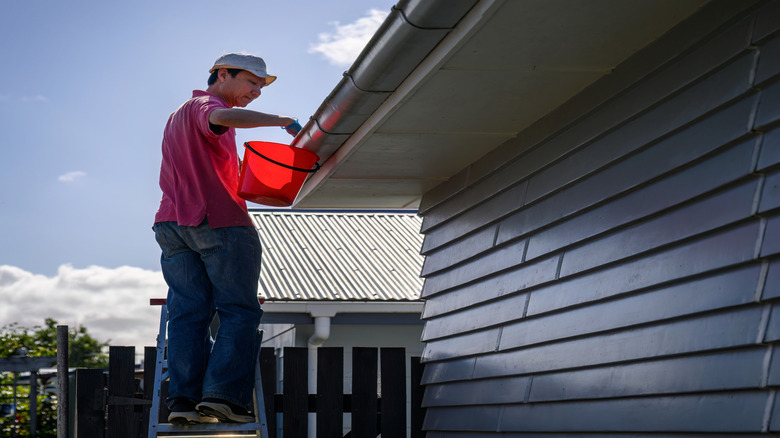 Man holding red bucket in front of gutters