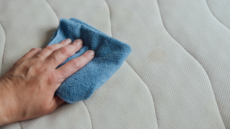 person cleaning mattress with cloth