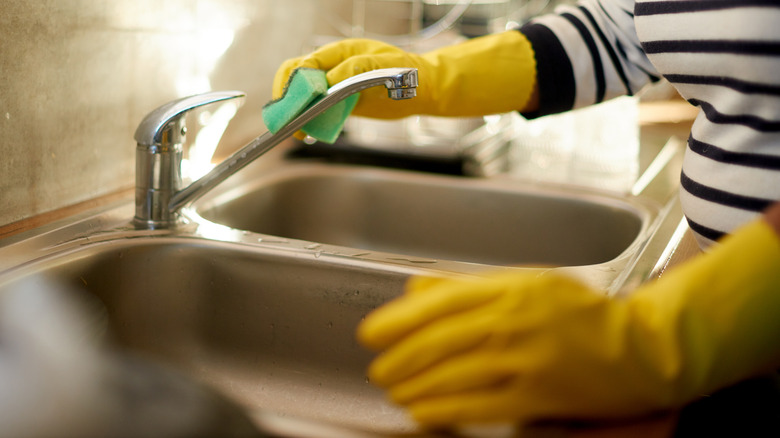 person wiping sink faucet