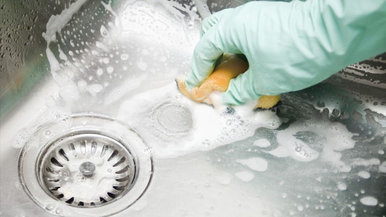 person scrubbing sink with sponge