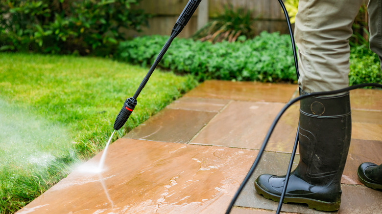 A person in work boots and pants powerwashing patio pavers