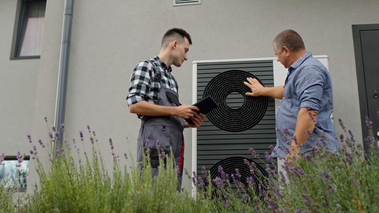 Two people inspecting heat pump outside of building