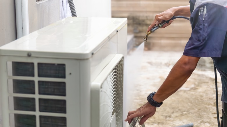 Man cleaning outdoor air conditioning unit with hose