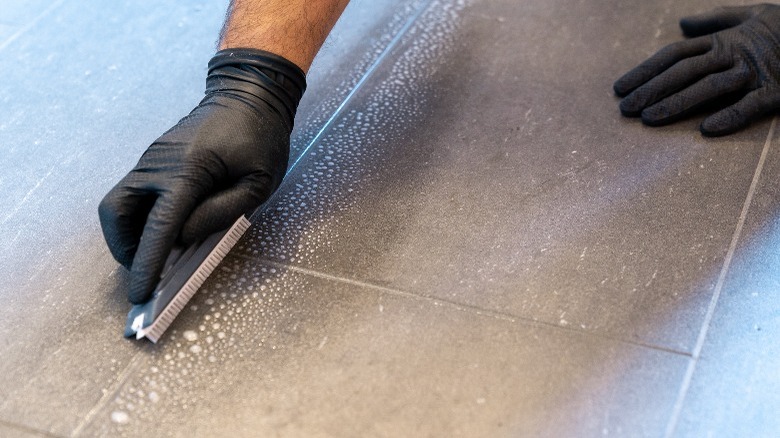 Black-gloved hand cleaning grout