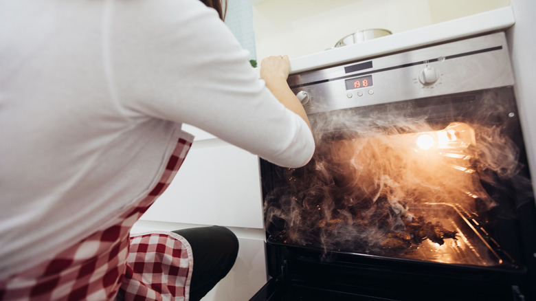 Woman opening smoky oven 