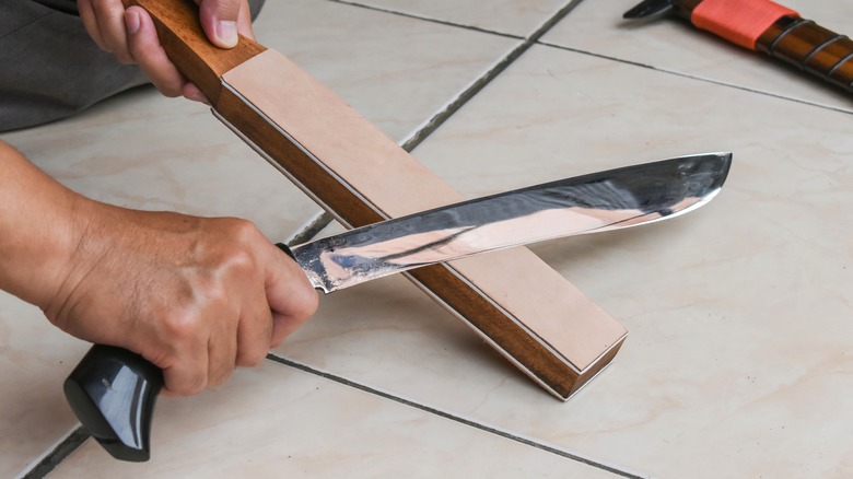 A man sharpens his machete using a stone