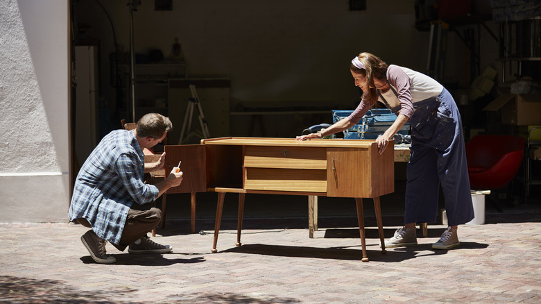 Two people refinishing a mid-century modern console table