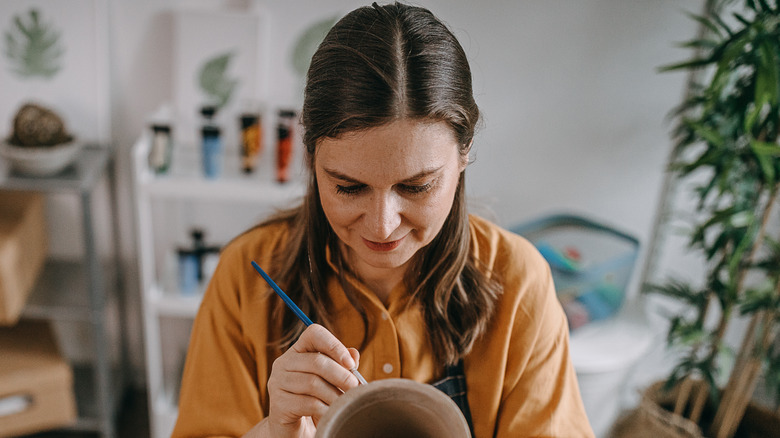 Focused woman painting brown vase with small brush