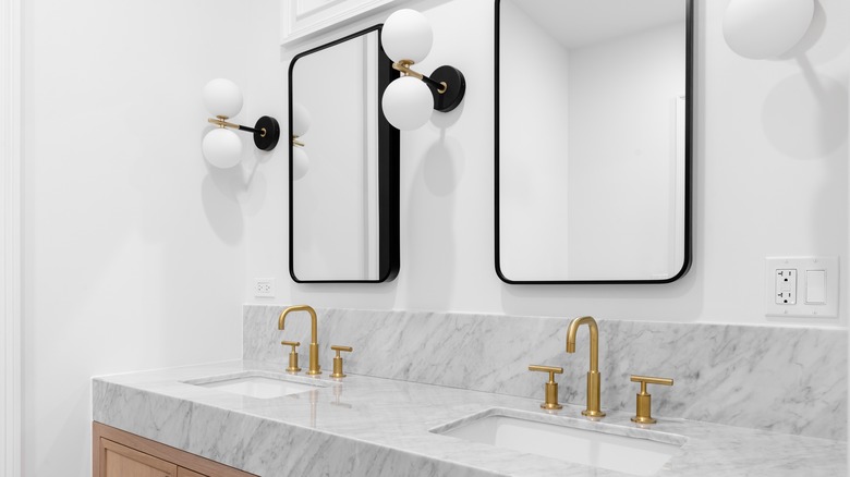 Bathroom with brass faucets and matte black and brass globe wall lights