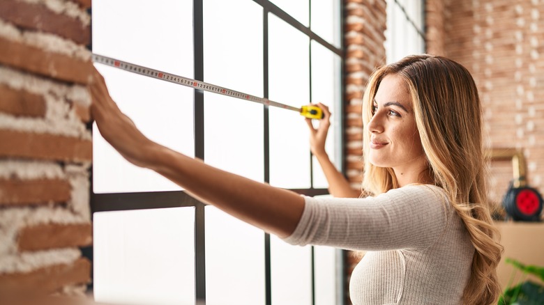 A blonde woman measures the width of a window