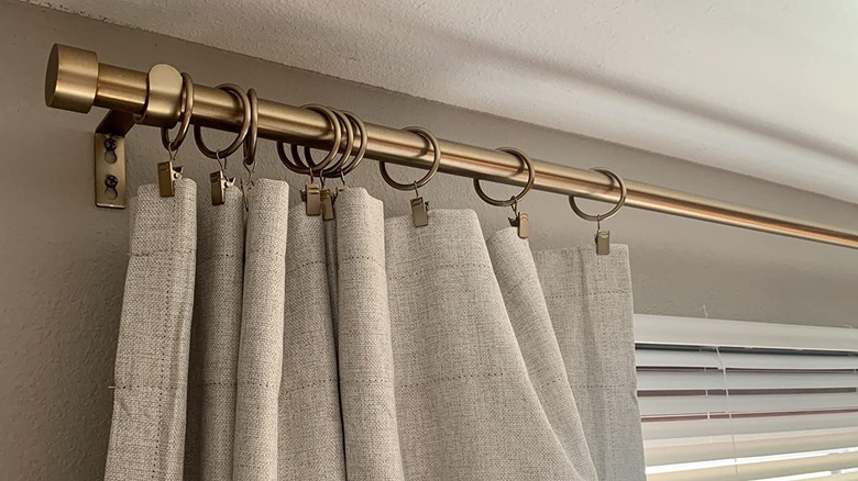 Neutral curtains hang from a gold curtain rod and clips