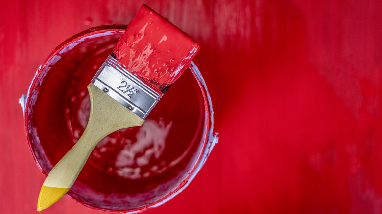 A red paint-coated paint brush bristle is atop a container of red paint.