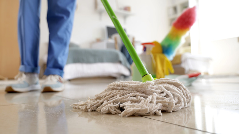 Person mopping a floor with a white mop head and green handle