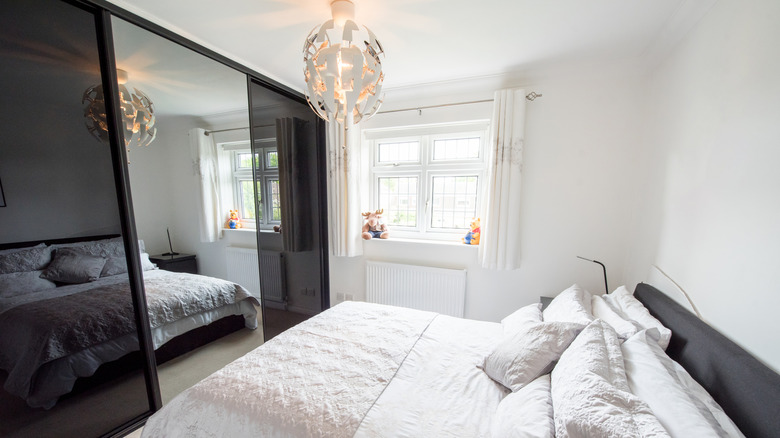 Bedroom with black and mirrored closet doors, small modern chandelier, and small window