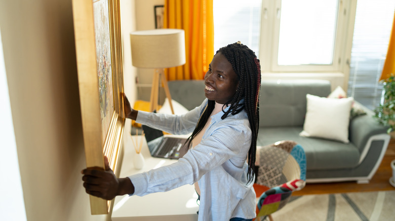 woman hanging picture on wall