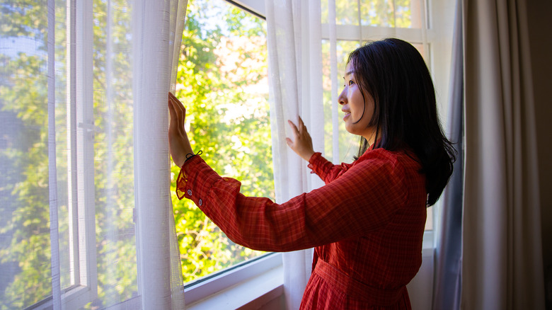 woman opening curtains on window