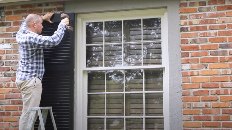 man installing window shutter