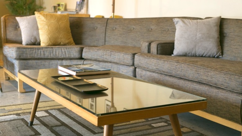 Gray upholstered mid-century boomerang sofa with glass-top cocktail table