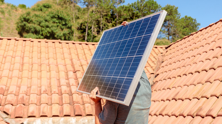 Person carries a solar panel to the top of a red-tiled roof