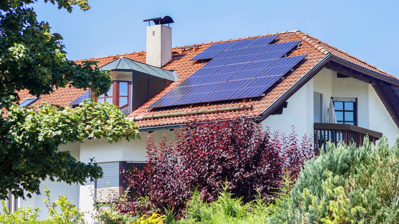 A white house with a red roof has solar panels installed