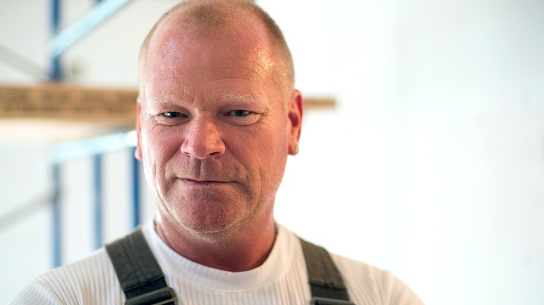 Mike Holmes in house undergoing remodel, looking at the camera with a smirk.