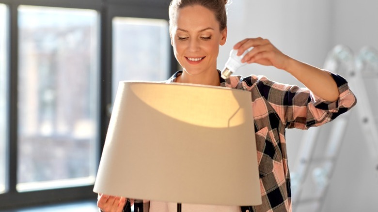 smiling woman putting new lightbulb in floor lamp